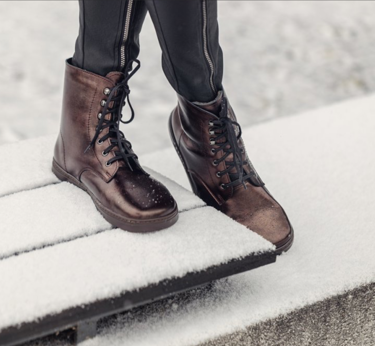 Barfußstiefel mit Schnürverschluss am Fuß getragen, breiter Zehenbox und flacher Sohle, geschlossener Fersenbereich, schräge Vorderansicht