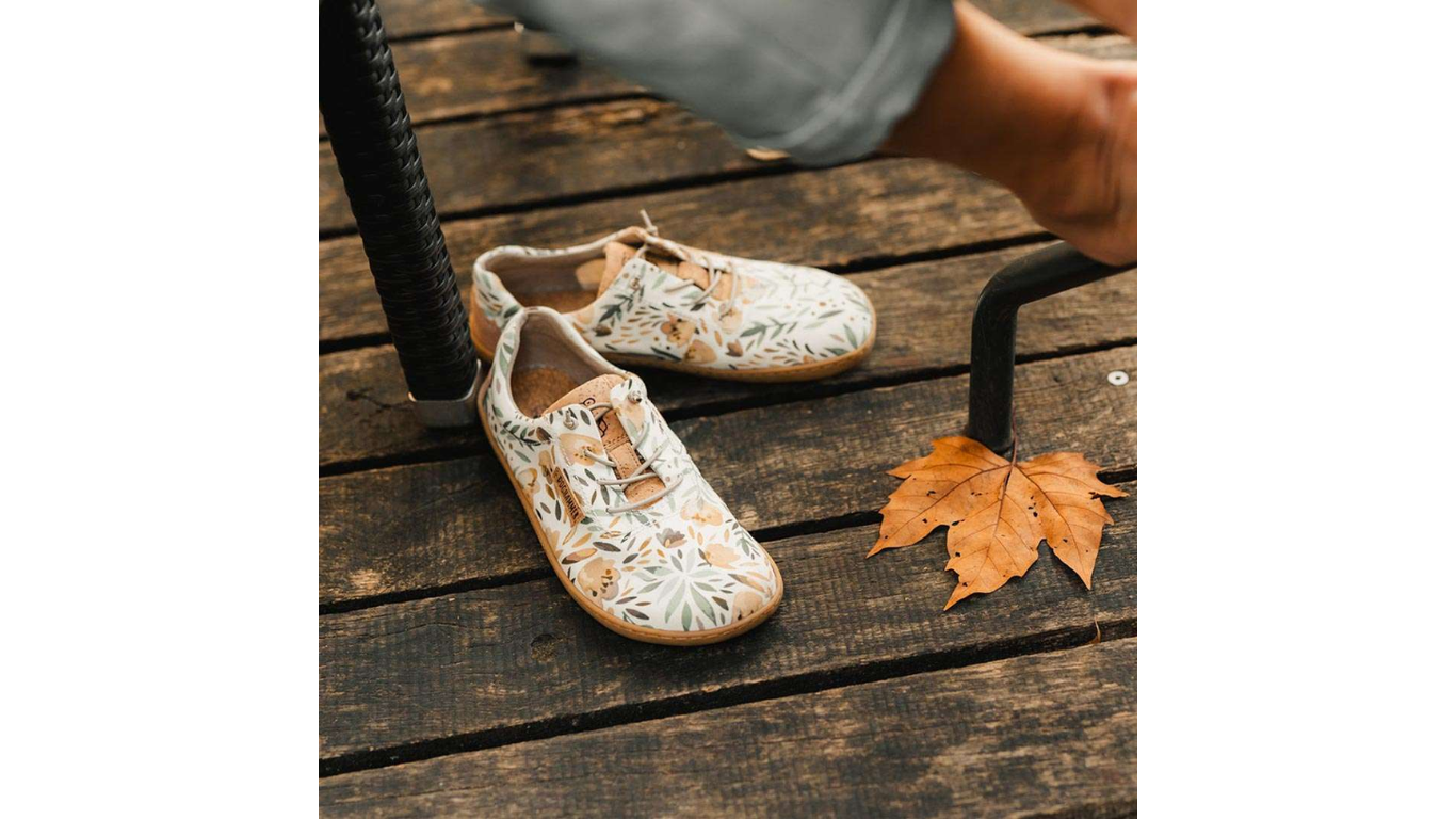 Barfußschuh mit geschlossener Zehenbox und Schnürung, am Fuß getragen auf Holzuntergrund. Schräge Vorderansicht.