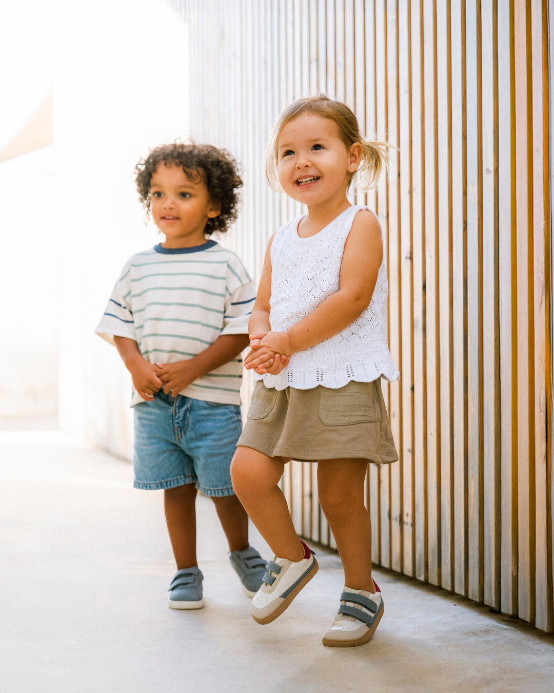 Barfußschuh für Kinder, breite Zehenbox, geschlossene Zehenpartie, geschlossener Fersenbereich, zwei Klettverschlüsse, flache Sohle, schräge Vorderansicht als Paar, getragen am Fuß