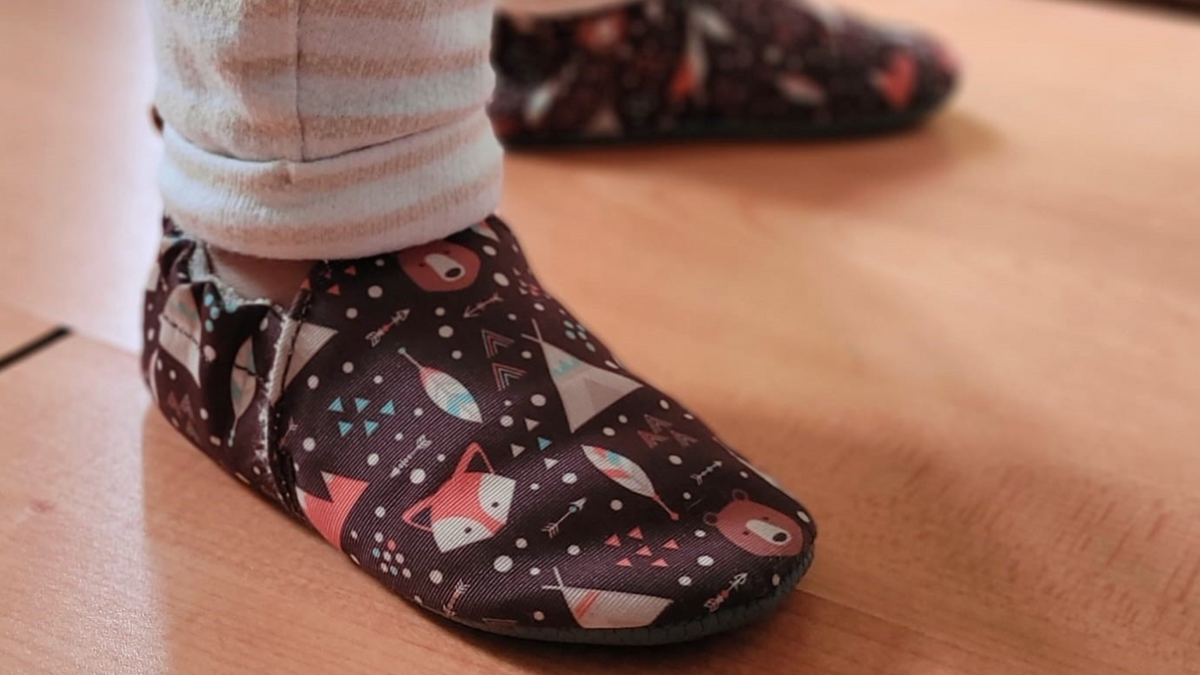Kinder Barfußhausschuh mit breiter Zehenbox und elastischem Einstieg, geschlossene Zehen und geschlossener Fersenbereich, einzelner Schuh, schräge Vorderansicht, am Fuß getragen