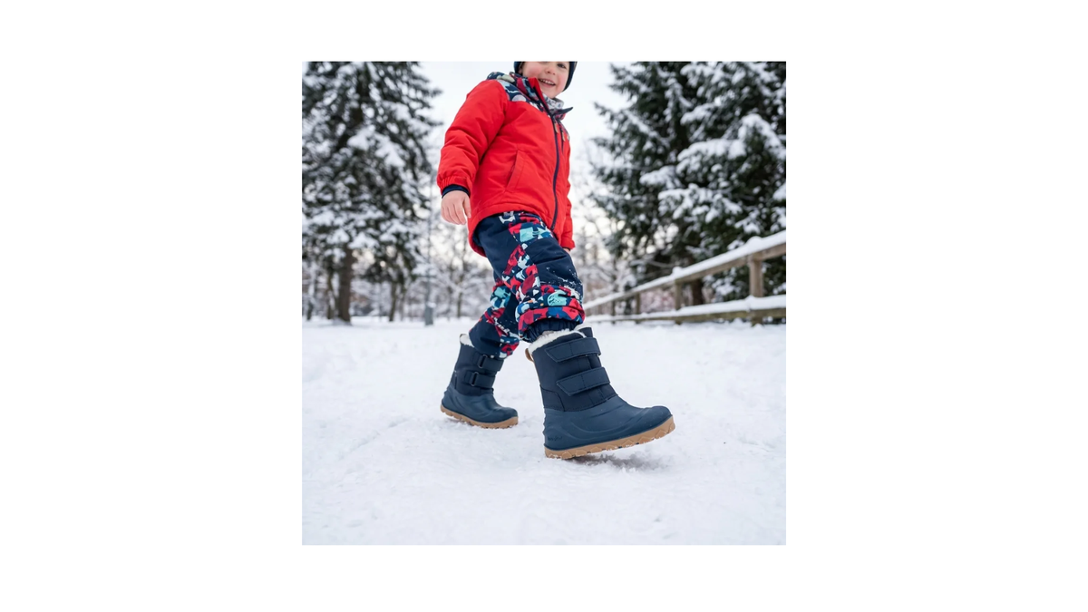 1. Kinder-Barfußwinterstiefel mit zwei Klettverschlüssen und hohem Schaft, am Fuß im Schnee getragen, Seitenansicht außen