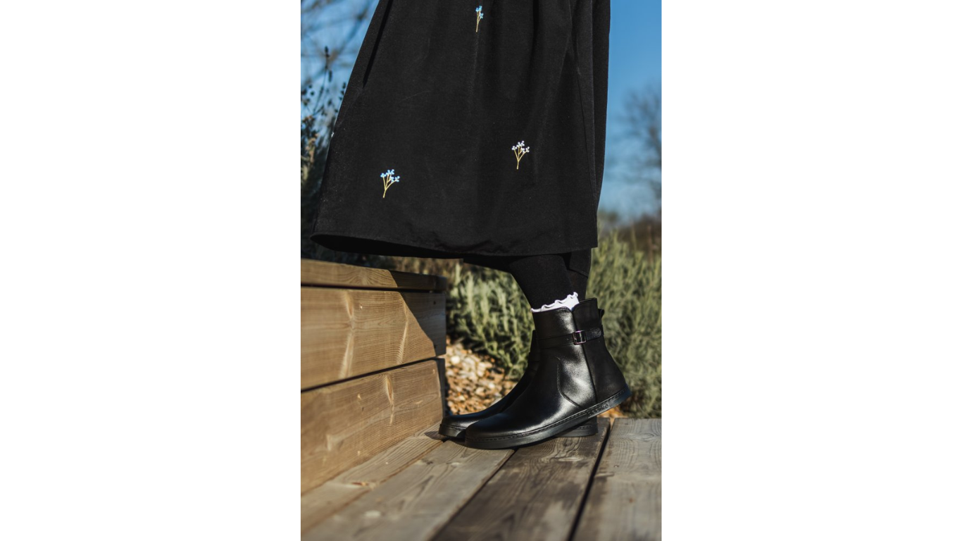 Barfußstiefel am Fuß getragen mit seitlichem Reißverschluss und Riemen, breiter Zehenbox und flacher Sohle, geschlossener Fersenbereich, schräge Vorderansicht