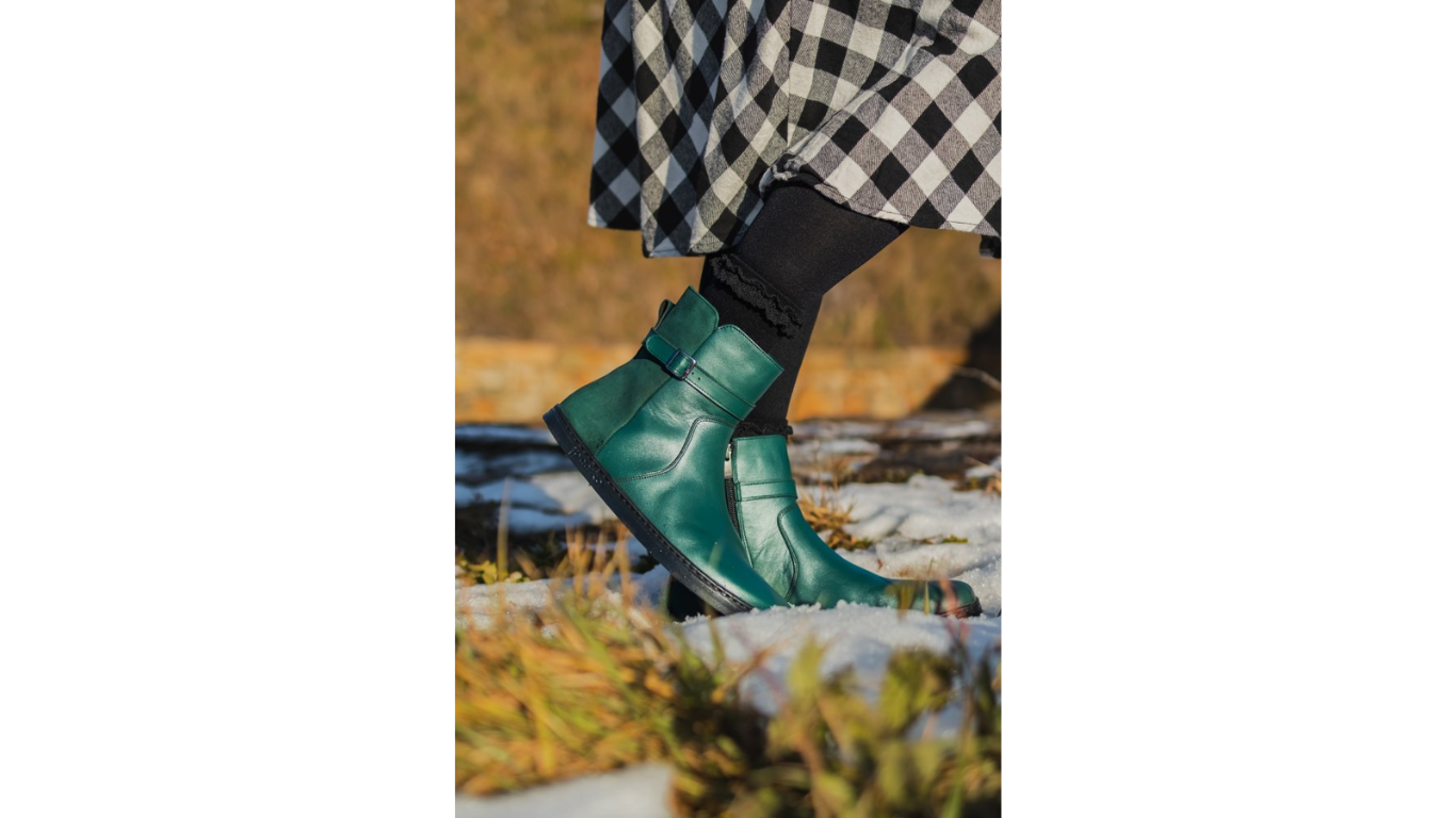 Barfußstiefel am Fuß getragen mit seitlichem Reißverschluss und Riemen, breiter Zehenbox und flacher Sohle, geschlossener Fersenbereich, schräge Vorderansicht