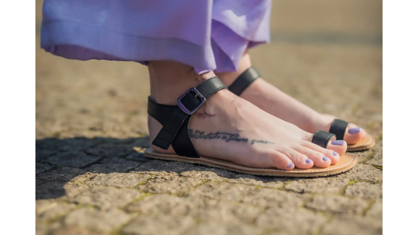 Sandalen im getragenen Zustand, Detailansicht der Füße im Stand. Offene Zehen, flache Sohle, bodennaher Kontakt.