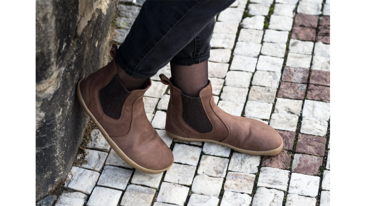 Barfußstiefel im getragenen Zustand, schräge Vorderansicht. Knöchelhoher Schaft, elastischer Seiteneinsatz, natürlicher Stand.