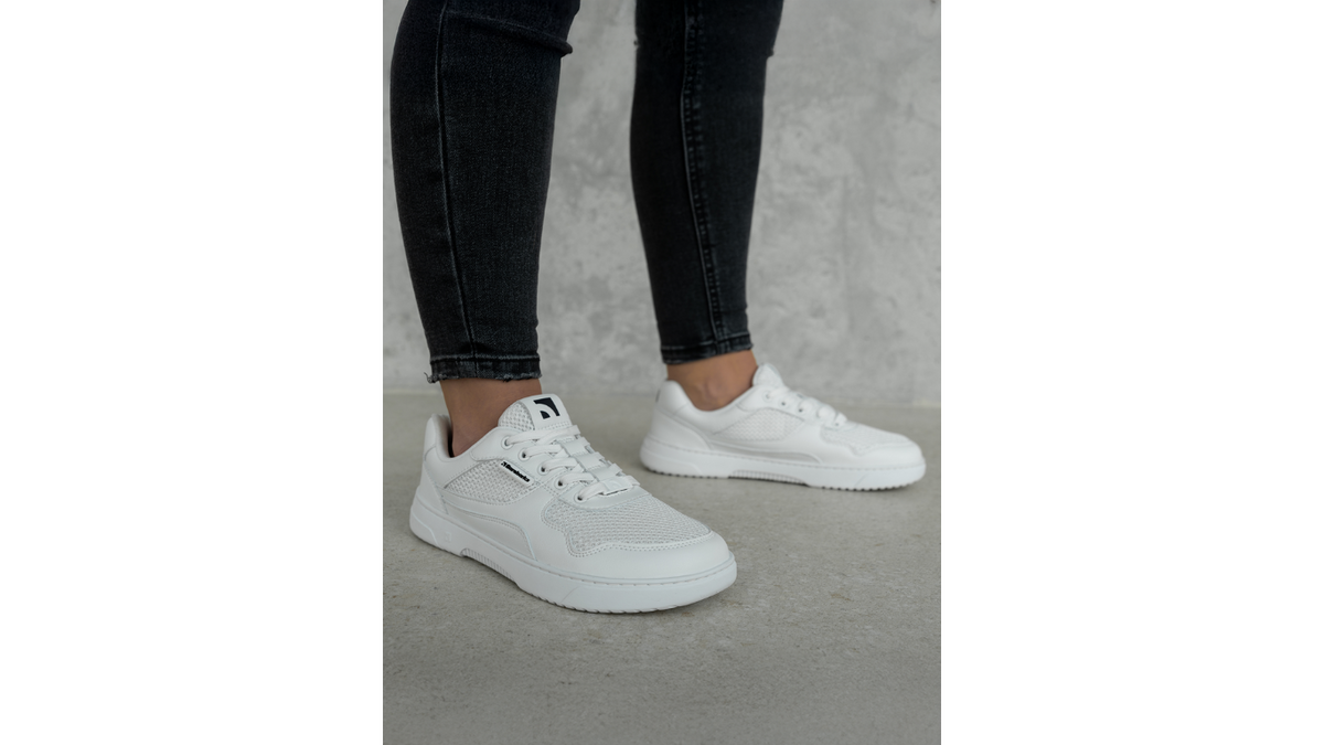 Barebarics Zing Fresh All White am Fuß getragen, Seitenansicht im Stand, weißer Sneaker mit Mesh-Einsätzen und flacher Sohle auf Betonboden.