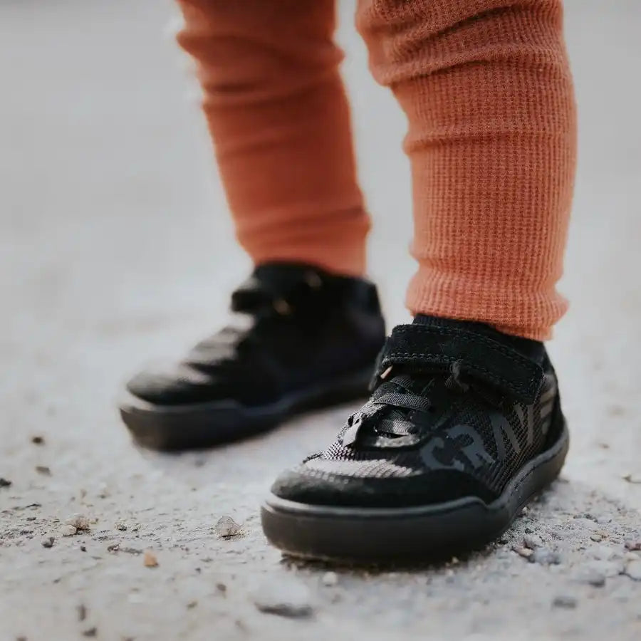 Barfußschuh für Kinder am Fuß getragen, mit Klettverschluss und Schnürung, breite Zehenbox erkennbar, geschlossene Zehen und Ferse, schräge Vorderansicht
