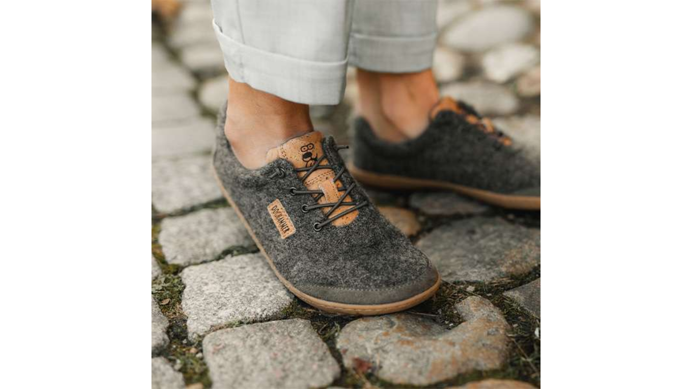Barfußschuhe für Erwachsene am Fuß getragen, graues Filz-Obermaterial, flache Sohle. Ansicht von oben auf Kopfsteinpflaster.
