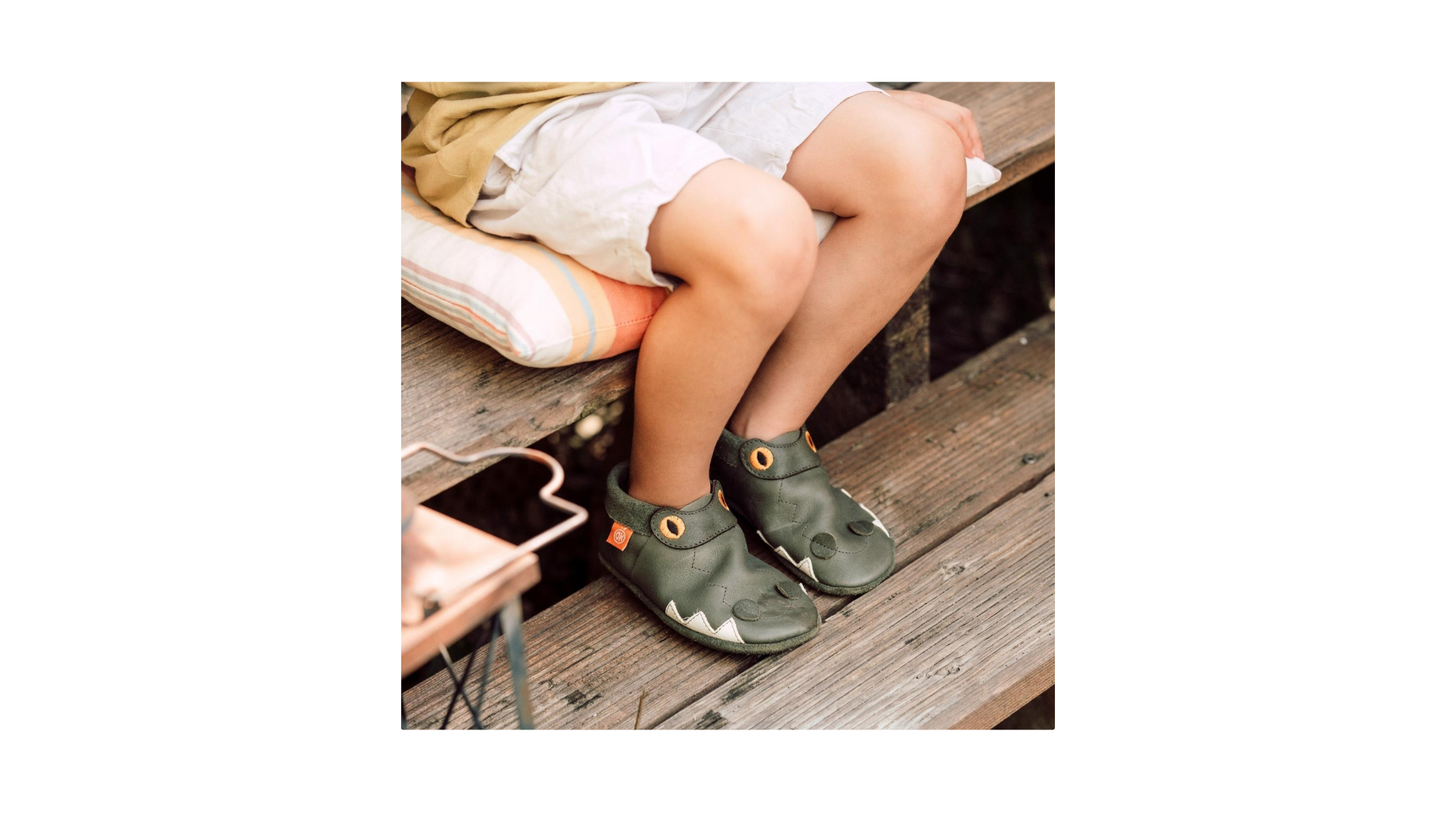 Kinderkrabbelschuhe mit Tiermotiv an den Füßen eines sitzenden Kindes, schräge Vorderansicht