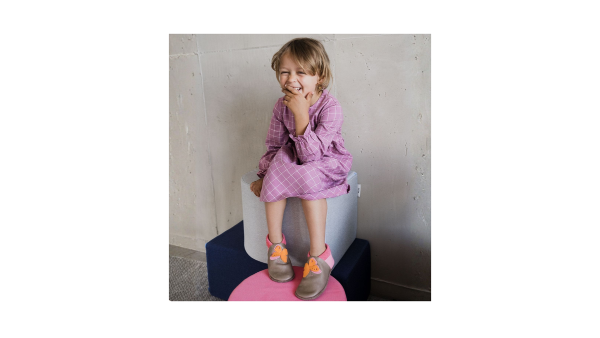 Kinderkrabbelschuhe mit Tiermotiv an den Füßen eines sitzenden Kindes, schräge Vorderansicht