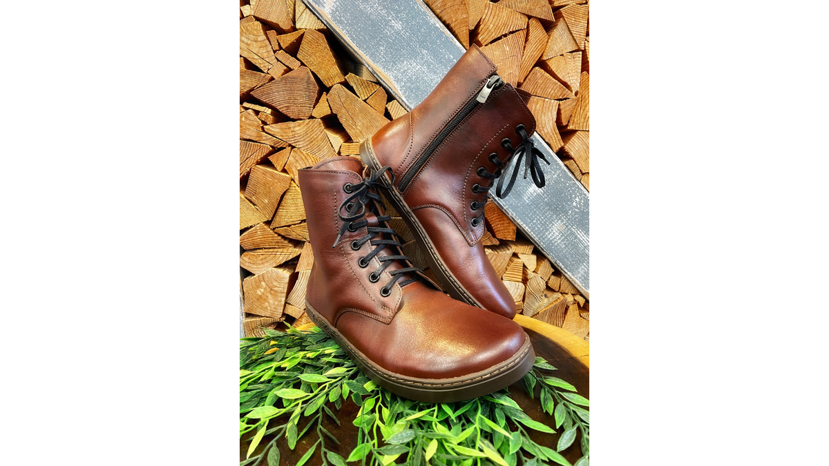 Barfußstiefel mit Schnürverschluss am Fuß getragen, breiter Zehenbox und flacher Sohle, geschlossener Fersenbereich, schräge Vorderansicht