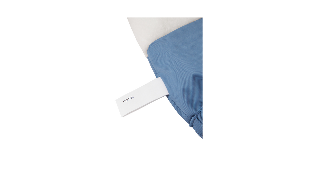 Hellblaue Baby-Überziehschuhe von Reima aus wasserabweisendem Material mit schwarzer Sohle und verstellbarem Gummizug. Detailfoto: Namenschild