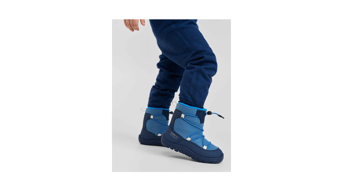Kinder-Barfußwinterstiefel mit Schnellverschluss und profilierter Sohle am Fuß getragen, Seitenansicht außen