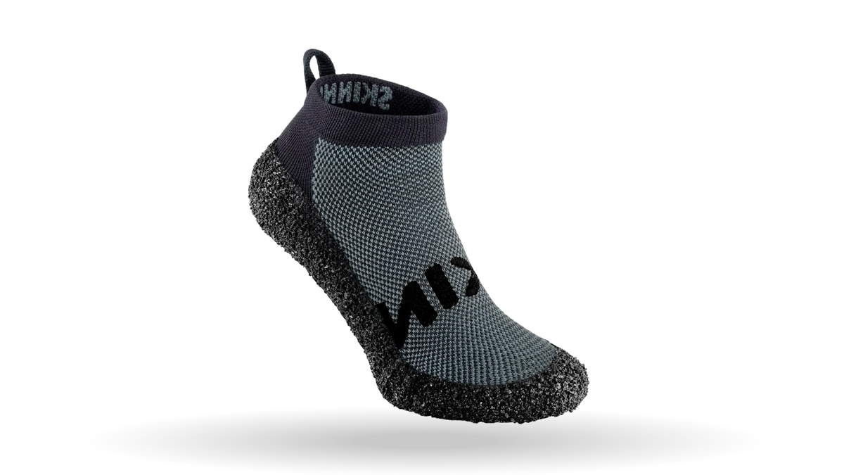 Skinners 2.0 in concrete, sockenähnlicher Schuh mit hellroter Strickoberfläche, grauem Skinners Schriftzug und schwarzer, flexibler Sohle in Seitenansicht.