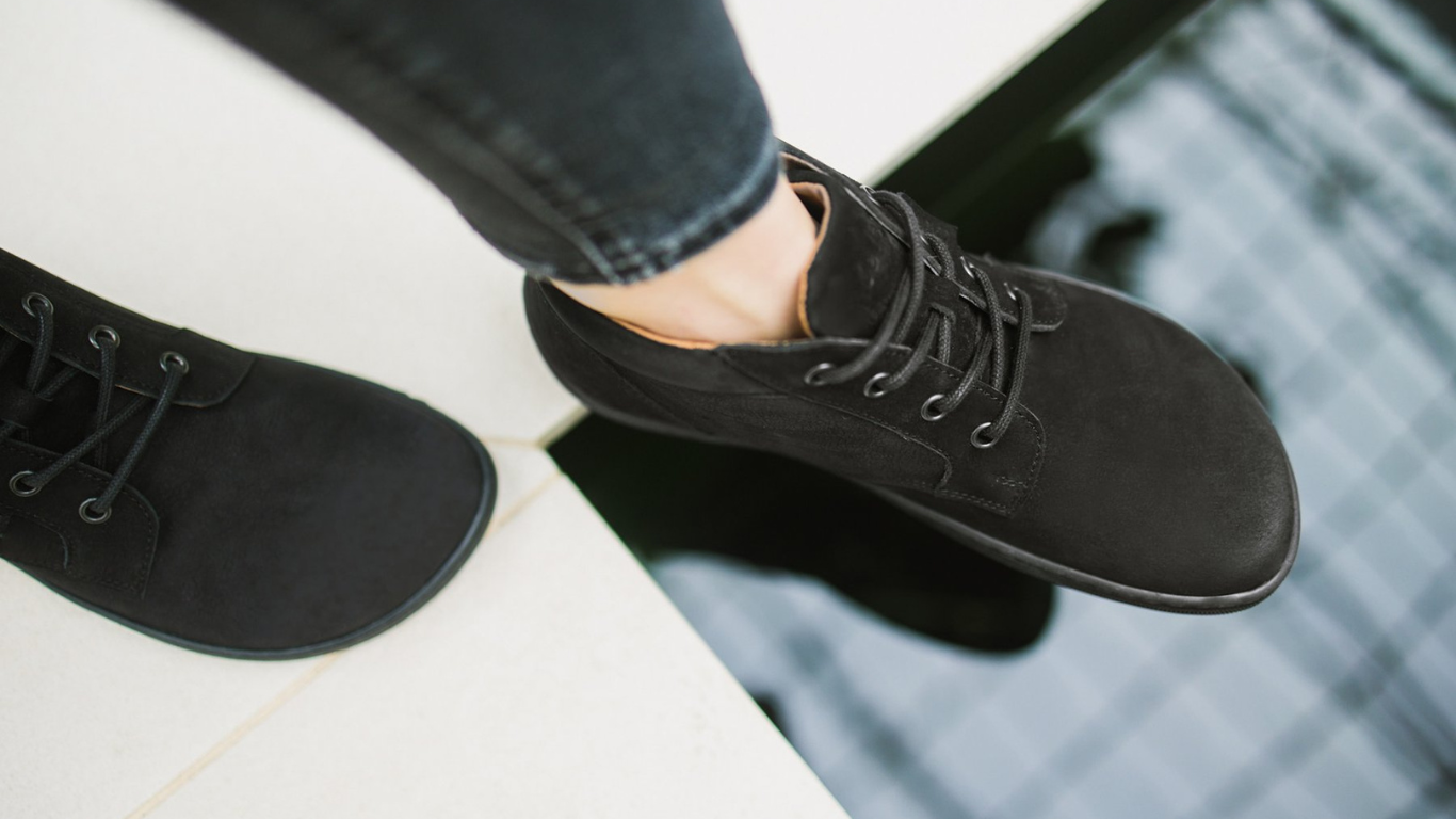 Knöchelhoher Barfußschuh für Erwachsene am Fuß getragen mit Schnürung und geschlossener Zehenbox, schräge Vorderansicht.