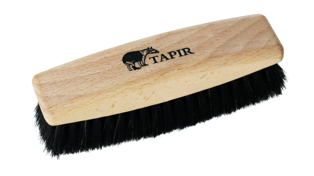 Schuhbürste mit Holzgriff und dichtem Borstenfeld, Logoaufdruck auf dem Griff, schräge Vorderansicht