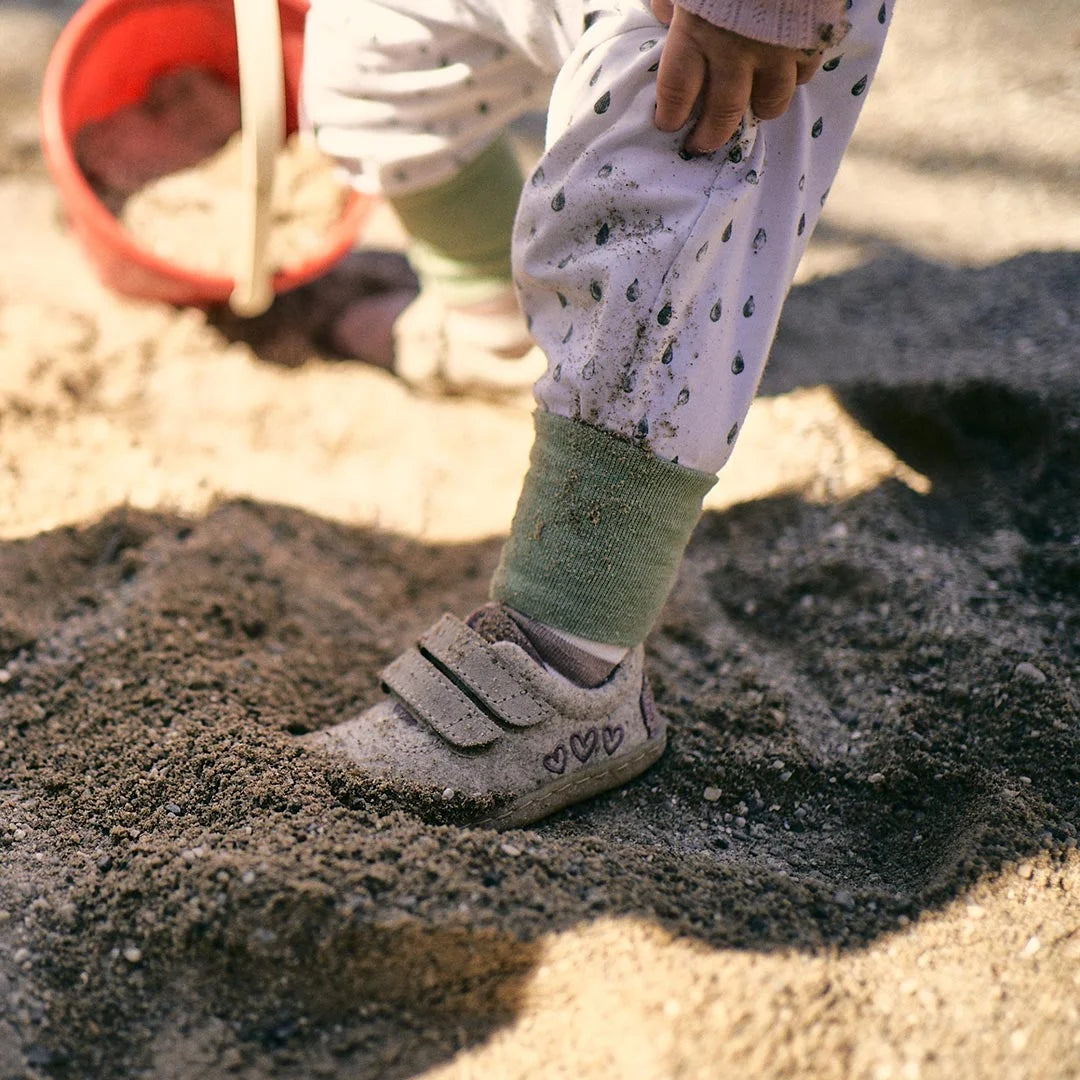 Barfußschuh für Kinder mit geschlossener Zehenbox und Klettverschlüssen, am Fuß getragen im Sand. Schräge Vorderansicht.