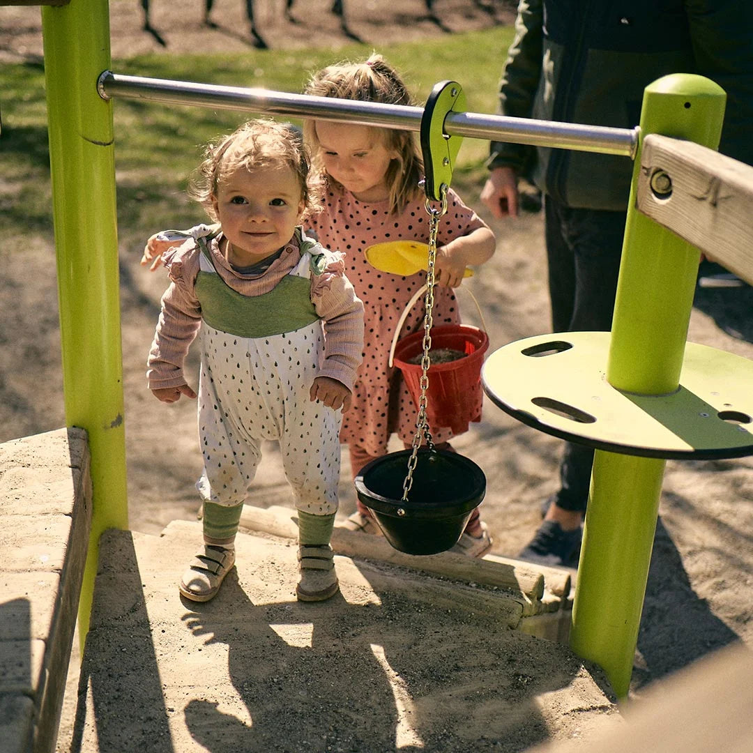 Barfußschuh für Kinder mit geschlossener Zehenbox und Klettverschlüssen, am Fuß getragen auf Spielgerät. Schräge Vorderansicht.