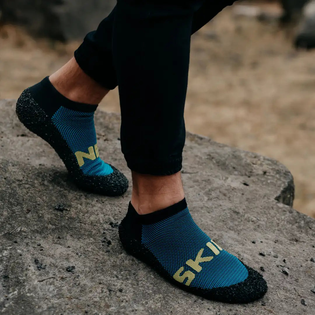 Skinners Socken in Schwarz mit blauem Muster und gelbem Logo, getragen auf Fels im Außenbereich.